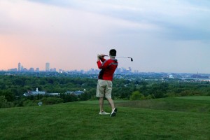 Golfer swinging club with city in background summer golf tournaments